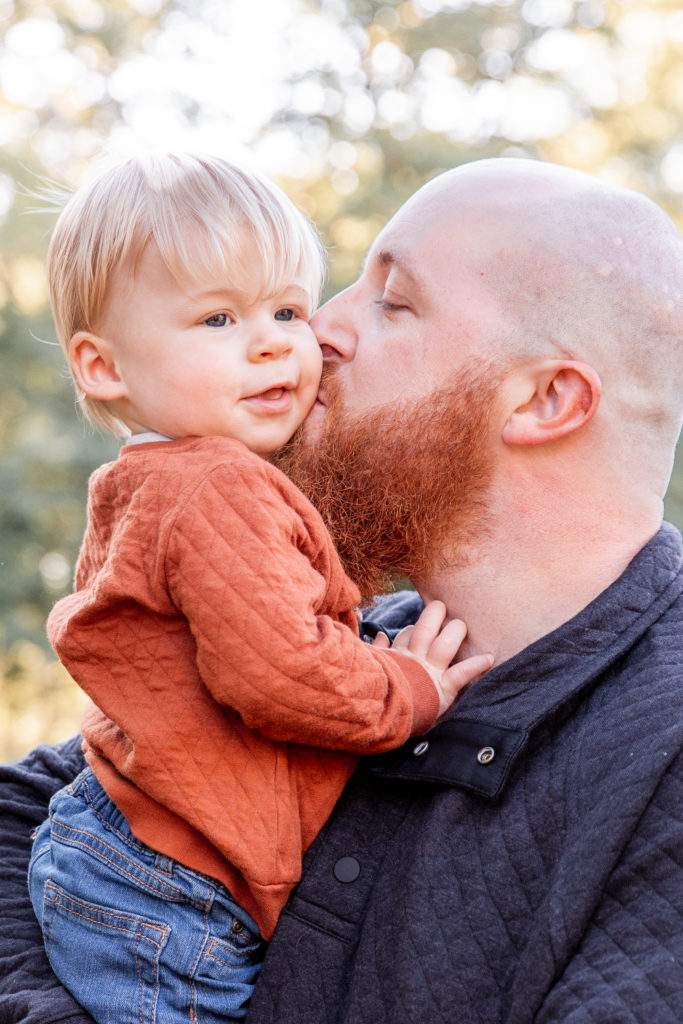 father kissing son on the cheek while he smiles in field