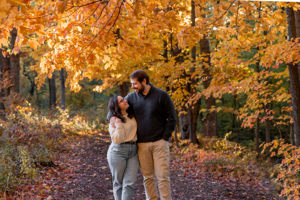 photograph of couple walking down path in the forest during the fall